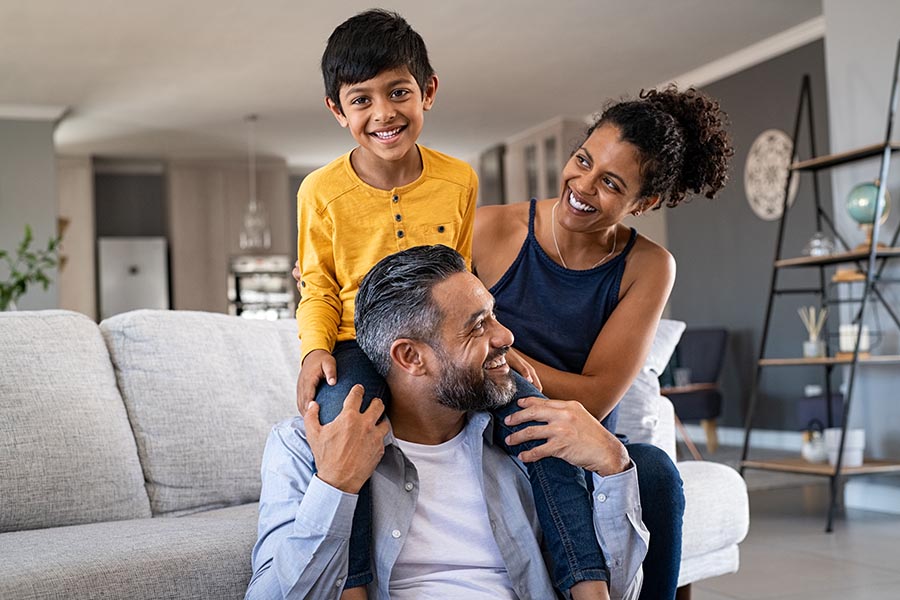 About Our Agency - Happy Family in Their Nice Living Room Plays on the Floor in Front of a Gray Couch