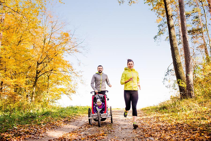 Blog - Parents Jog With Their Baby in a Jogging Stroller, Along a Leaf-Lined Path Through the Woods in the Fall