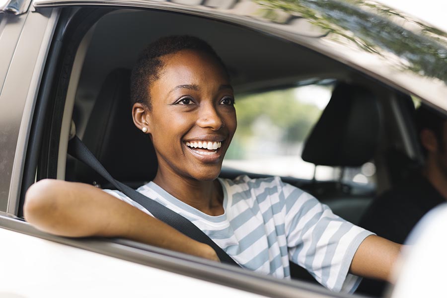Contact Us - Woman Smiles in the Passenger Seat of a Silver Car, Resting Her Elbow on the Window