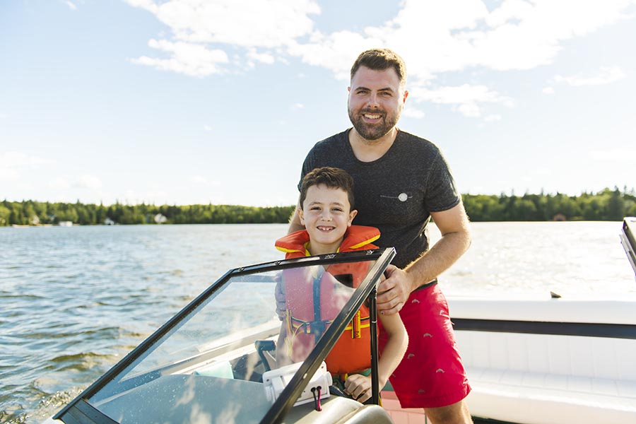 Personal Insurance - Father and Son Stand at the Controls of Their Boat on a Calm Lake, Sun Shining
